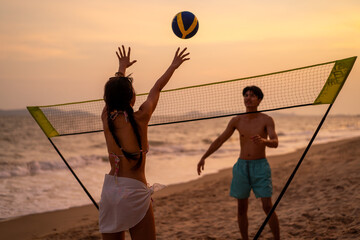 Asian young lovely couple playing volley on the beach during senset. 