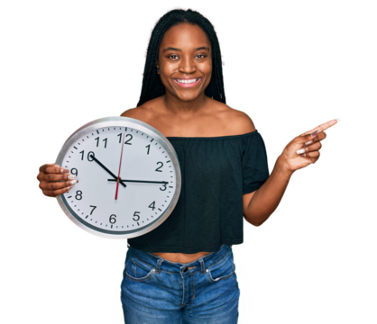 Young african american woman holding big clock smiling happy pointing with hand and finger to the side