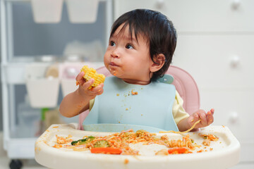 infant baby eating food and vegetable by self feeding BLW or baby led weaning on chair