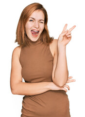 Young caucasian woman wearing casual clothes smiling with happy face winking at the camera doing victory sign. number two.