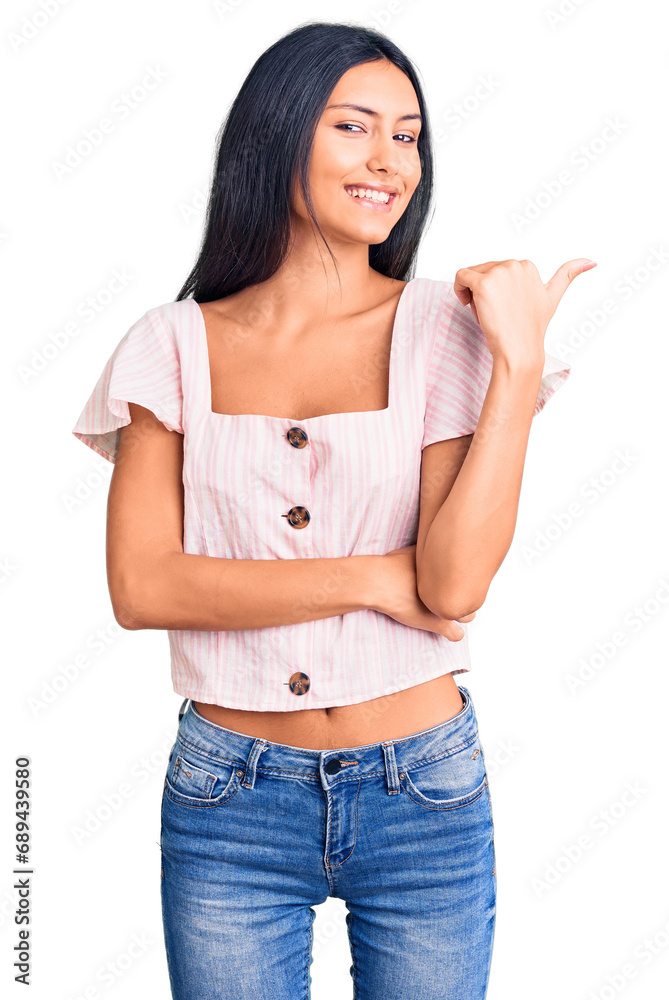 Sticker Young beautiful latin girl wearing casual clothes smiling with happy face looking and pointing to the side with thumb up.