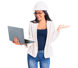 Young beautiful latin girl wearing architect hardhat holding laptop celebrating victory with happy smile and winner expression with raised hands