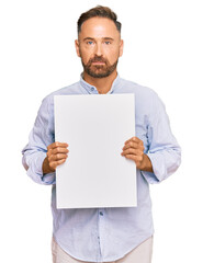 Handsome middle age man holding blank empty banner thinking attitude and sober expression looking self confident