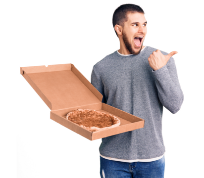 Young handsome man holding delivery italian pizza pointing thumb up to the side smiling happy with open mouth
