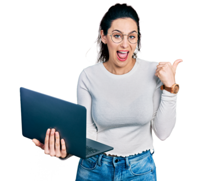 Young hispanic woman working using computer laptop pointing thumb up to the side smiling happy with open mouth