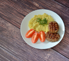 Two meat fried cutlets with mashed potatoes, dill and tomato on a wooden table.