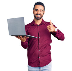 Young hispanic man holding laptop smiling happy and positive, thumb up doing excellent and approval sign