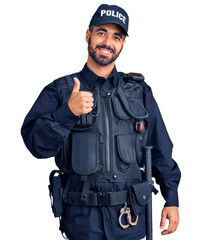 Young hispanic man wearing police uniform doing happy thumbs up gesture with hand. approving expression looking at the camera showing success.