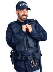 Young hispanic man wearing police uniform laughing nervous and excited with hands on chin looking to the side
