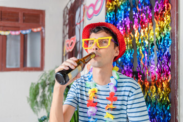 Brazilian man joyfully celebrates Carnival at home, sipping beer amidst festive decor. Ideal image to capture the spirit of people reveling in the joy of Carnival festivities