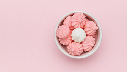 White and pink meringue in a white ceramic bowl on a pink background. Space for text.