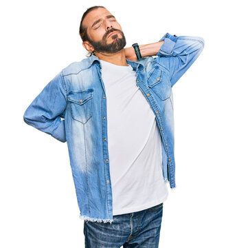 Attractive man with long hair and beard wearing casual denim jacket suffering of neck ache injury, touching neck with hand, muscular pain