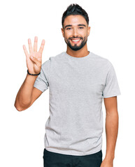 Young man with beard wearing casual grey tshirt showing and pointing up with fingers number four while smiling confident and happy.