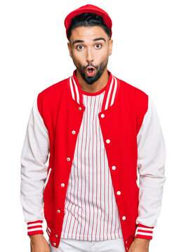 Young man with beard wearing baseball uniform afraid and shocked with surprise expression, fear and excited face.