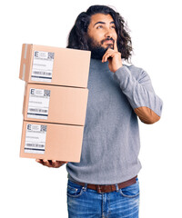 Young arab man holding delivery package serious face thinking about question with hand on chin,...