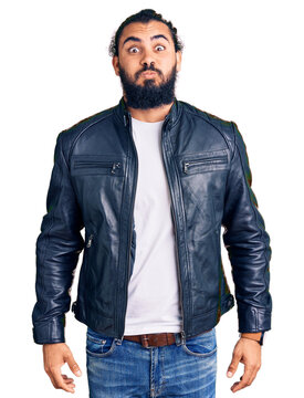 Young arab man wearing casual leather jacket puffing cheeks with funny face. mouth inflated with air, crazy expression.