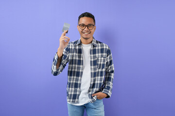Portrait of a smiling Asian man with a credit card in his hand. Non-cash payment concept and...
