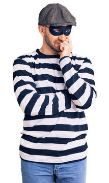 Young handsome man wearing burglar mask looking stressed and nervous with hands on mouth biting nails. anxiety problem.