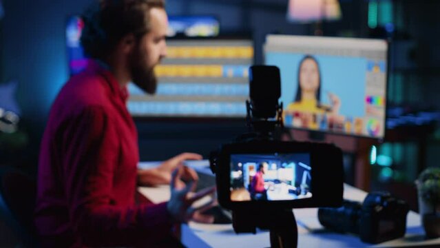 Content creation equipment used by photo editor to film tutorial on selecting editorial pictures for fashion magazine. Focus on camera recording photographer in blurry background presenting his work