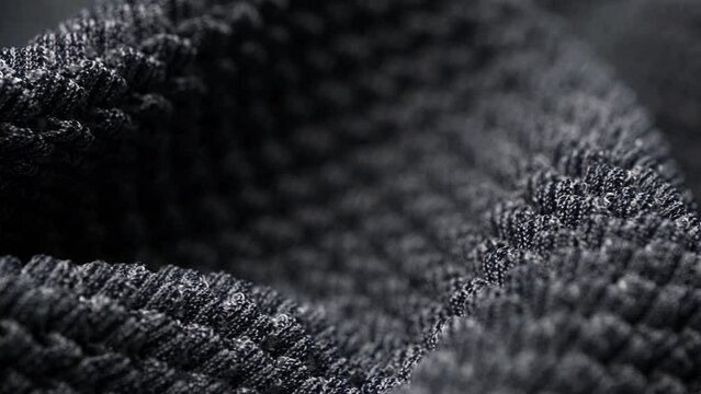 macro video of the folds of the rotating knitted textured boucle fabric in dark gray color. convex texture of the factory fabric. warm and cozy knitwear for cold winter. textile background.