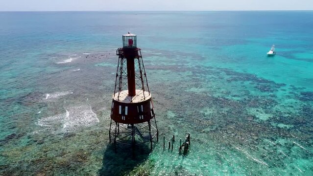 An 4K drone shot of an abandoned lighthouse, in a remote area of the Caribbean Sea, near Bimini, Bahamas. The camera rotates around the lighthouse, while slowly reversing away.