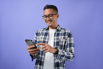 Photo of a young Asian man cheerful bristled guy holding a smartphone screen, wearing a shirt and isolated on a purple background.