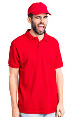 Young handsome man with beard wearing delivery uniform winking looking at the camera with sexy expression, cheerful and happy face.