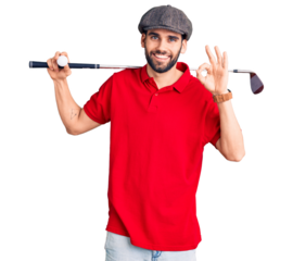 Young handsome man with beard playing golf holding club and ball doing ok sign with fingers, smiling friendly gesturing excellent symbol