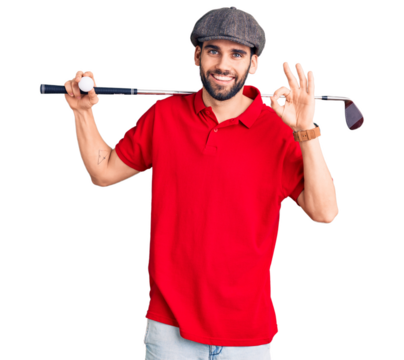 Young handsome man with beard playing golf holding club and ball doing ok sign with fingers, smiling friendly gesturing excellent symbol