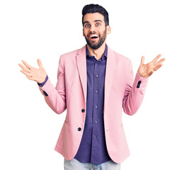 Young handsome man with beard wearing elegant jacket celebrating victory with happy smile and winner expression with raised hands