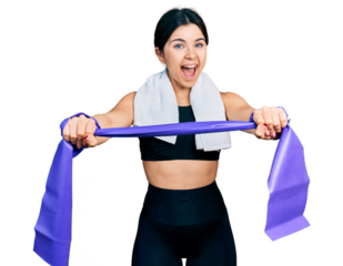 Young brunette woman with blue eyes training arm resistance with elastic arm bands celebrating crazy and amazed for success with open eyes screaming excited.