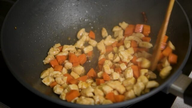 Cooking and stirring chopped chicken breast with carrots on non stick pan