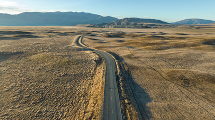 Drone  perspective of the rural and remote country road through arid tundra desert land to the snow...