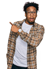 Young african american man with beard wearing casual clothes and glasses surprised pointing with finger to the side, open mouth amazed expression.