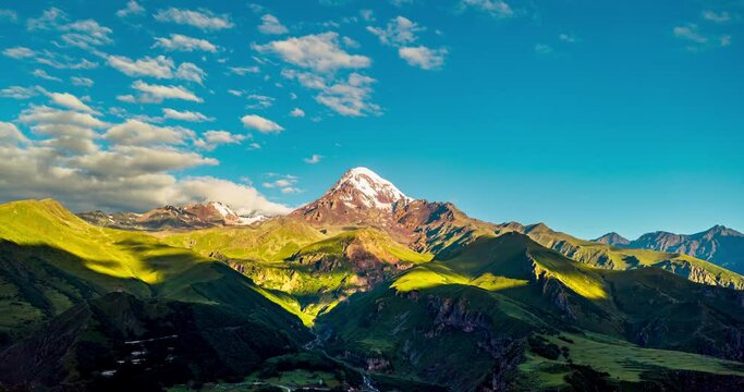 Aerial timelapse in the Kazbegi mountain of Georgia. A beautiful flight into the gorge between the mountains. Clouds float over a small town. Illustration of tourist mountain trekking routes.