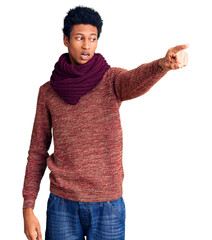 Young african american man wearing casual winter sweater and scarf pointing with finger surprised ahead, open mouth amazed expression, something on the front