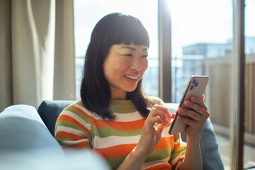 Happy smiling young woman using smartphone on home sofa