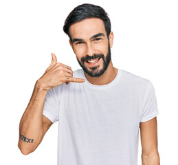 Young hispanic man wearing casual white t shirt smiling doing phone gesture with hand and fingers like talking on the telephone. communicating concepts.