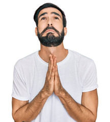 Young hispanic man wearing casual white t shirt begging and praying with hands together with hope expression on face very emotional and worried. begging.