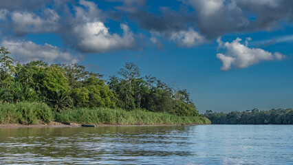 A calm river in the rain forest. Ripples on the shiny water. Lush tropical vegetation on the shore. The boats are moored. Clouds in the blue sky. Malaysia. Borneo. Kinabatangan River