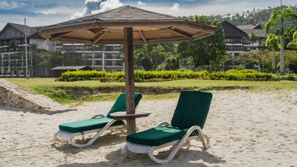 A relaxation area on the beach. Two chaise lounges with soft mattresses stand on the sand in the...