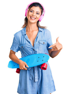 Young beautiful woman wearing headphones and holding skate smiling happy pointing with hand and finger