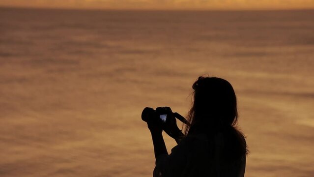Handheld footage of silhouette of female capturing images at sunset
