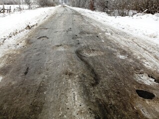 A snowy road on which ice has formed on the carriageway. Many icy pits on the road.