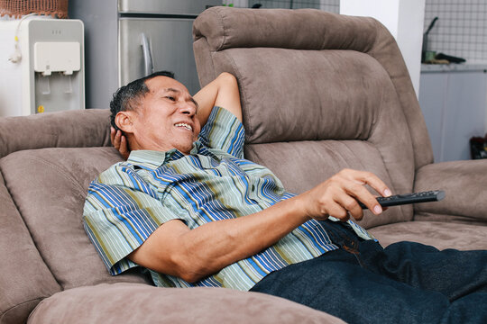 Portrait of happy senior Asian man lying on couch watching television at home