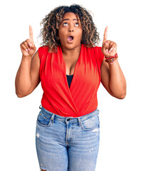 Young african american plus size woman wearing casual style with sleeveless shirt amazed and surprised looking up and pointing with fingers and raised arms.