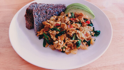A plate of scrambled eggs with spinach and avocado served with toast on a wooden table for breakfast, healthy diet and wellness at home
