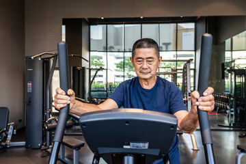 Fototapeta na wymiar Asian old man in the 70s or 80s to step on flywheel training helping leg muscle strength, Healthy older man training or a quick warm up in the fitness room. lifestyle or health of senior man