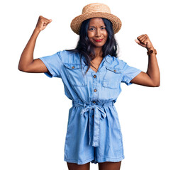 Young indian girl wearing summer hat showing arms muscles smiling proud. fitness concept.