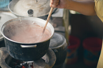Close-up of a hand stirring a pot of sikwate or Filipino hot chocolate drink in a traditional...